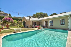 A swimming pool with a tiled edge, a patio with a bench, and a house with a covered porch. - Valley Heights Guest House B&B (Cape Town)