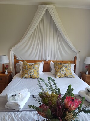 A neatly made bed with a canopy, two decorative pillows, a bedside table with a lamp, and a floral arrangement. - Valley Heights Guest House B&B (Cape Town)