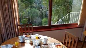 Ein Frühstückstisch mit Tellern, Tassen und Besteck, mit Blick auf Bäume und einem Geländer draußen.