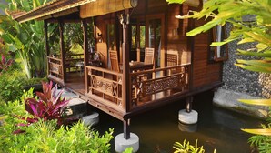 Una casa flotante de madera con balcón, rodeada de exuberante vegetación y un estanque.