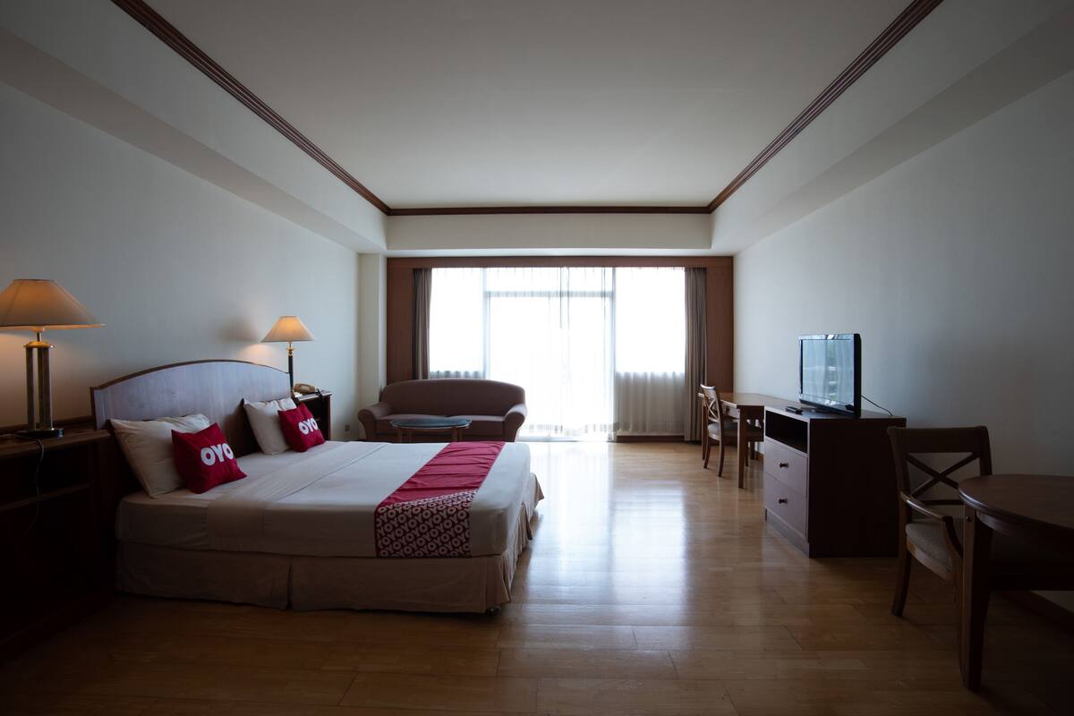 A hotel room with a bed, bedside lamps, a desk, a chair, and a television.