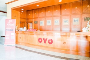 A reception desk with the OYO logo, framed pictures on the wall, and a pink sign advertising a 100% discount voucher. - Ayutthaya River View Hotel (Ayutthaya)