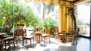 Un espacio interior amplio con varias mesas y sillas de madera, ventanas grandes con cortinas amarillas y vistas a zonas verdes.