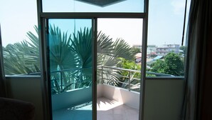 Un balcón con puerta de cristal, vistas a palmeras y un edificio al fondo.