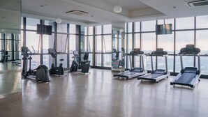 A gym with cardio machines, a mirrored wall, and large windows offering a city view. - Iconic Homestay (Kota Kinabalu)