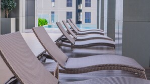 A row of wicker lounge chairs facing a swimming pool, with a modern building in the background. - Iconic Homestay (Kota Kinabalu)