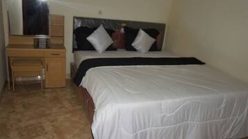 A bedroom with a bed, a wooden desk, and a mirror.