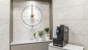 A modern bathroom with a marble wall, a wall-mounted clock, and a coffee machine on a counter. - JJ Hotel (Seongnam)