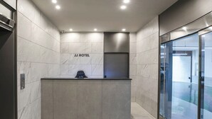 A modern hotel reception area with a marble wall, a reception desk, and a glass door leading to the lobby. - JJ Hotel (Seongnam)