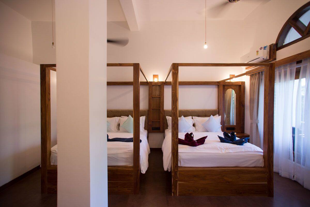 A hotel room with four single beds, wooden headboards, a large mirror, and a view of the outdoors through a window.