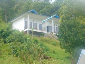 A two-story building with a flat roof, surrounded by greenery.