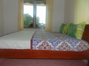 A bed with a patterned bedspread and pillows, a wooden headboard, and a window with curtains.