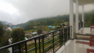 A balcony with a metal railing overlooking a village with houses and greenery.
