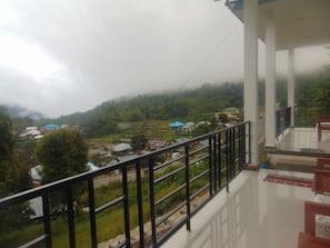 A balcony with a metal railing overlooking a village with houses and greenery.