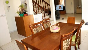 Un comedor con una mesa y sillas de madera, un televisor al fondo y una escalera que conduce a otra habitación.