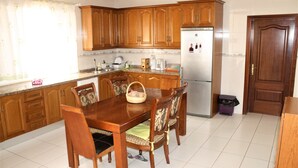 Una cocina con armarios de madera, un refrigerador de acero inoxidable, una mesa de comedor con sillas y una ventana con cortinas.