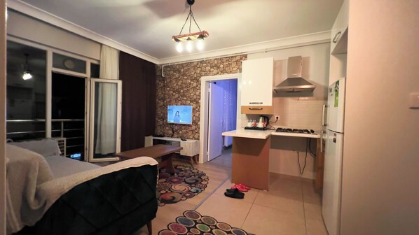 A compact hotel room with a bed, a small desk, a television, a kitchen area with a stove and refrigerator, and a stone accent wall. - Edirne House (Edirne)