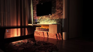 A room with a stone wall, a flat-screen TV mounted above a fireplace, and a patterned rug on the floor. - Edirne House (Edirne)