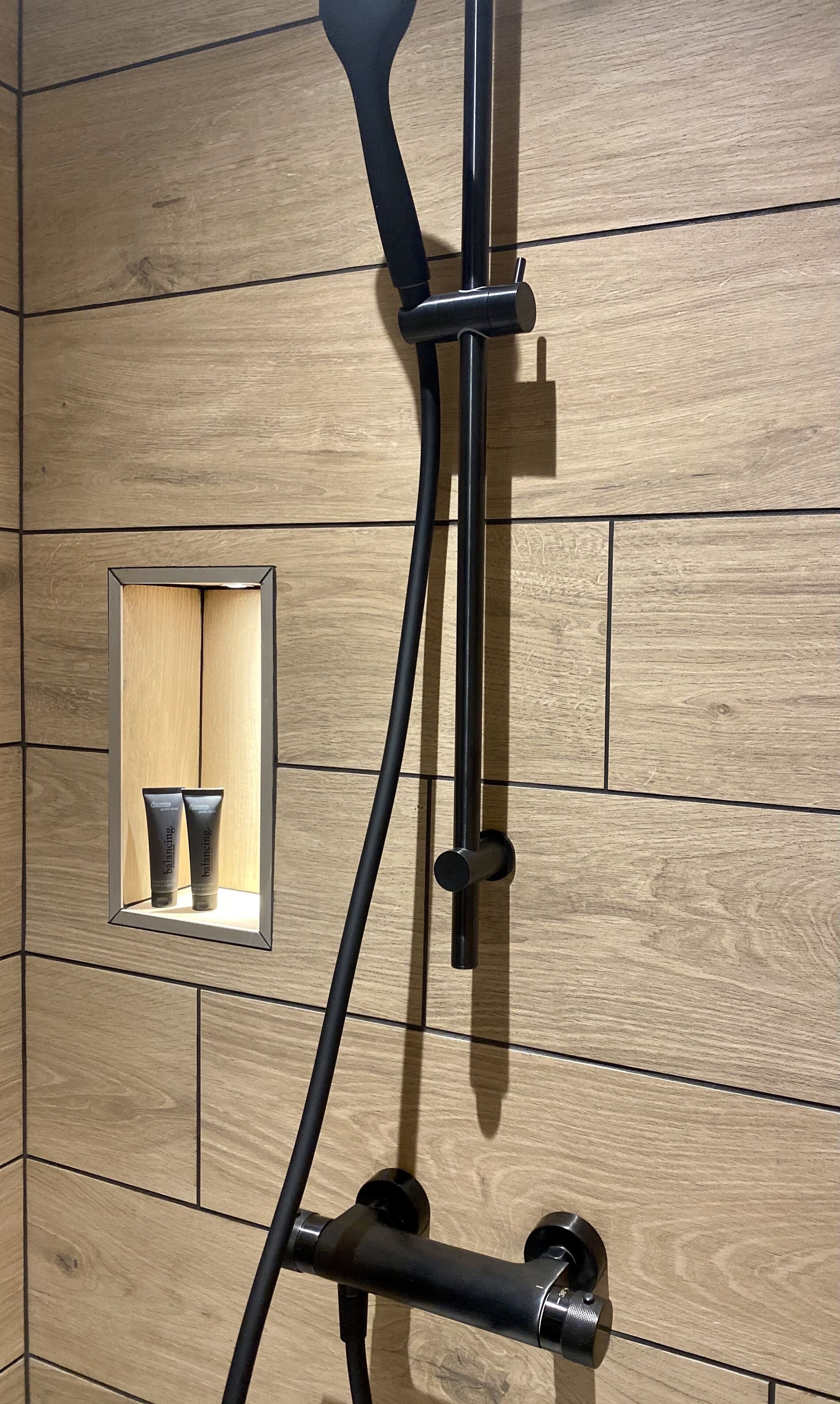 A shower with a wooden panel wall, a small mirror, and two bottles of shampoo.