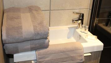 A bathroom with a white sink, a mirror, and a towel rack holding three towels.