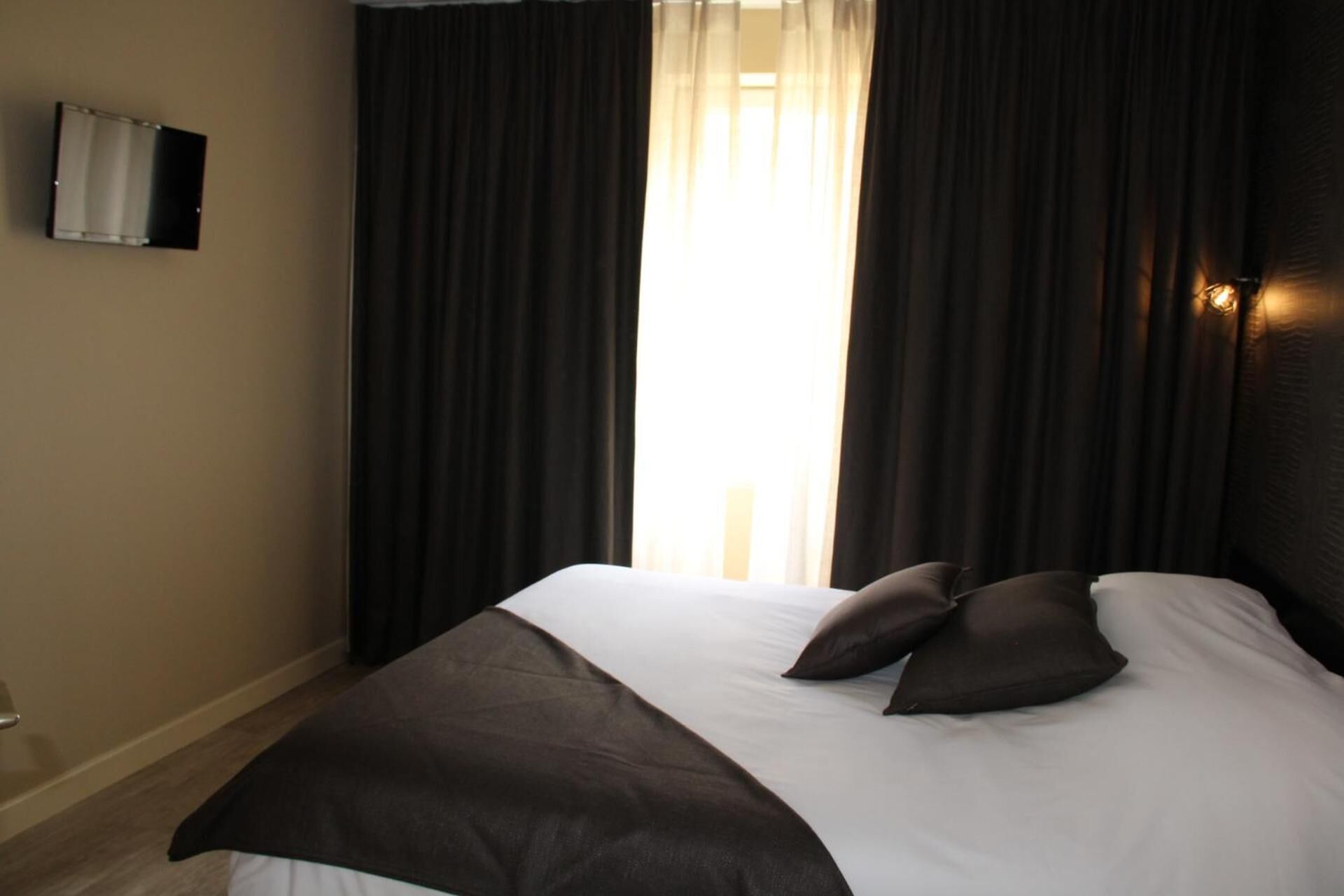 A hotel room with a large bed, dark curtains, and a wall-mounted TV.