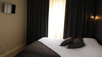 A hotel room with a large bed, dark curtains, and a wall-mounted TV.