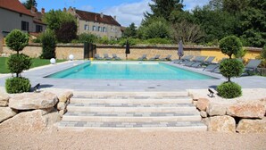 Una piscina rectangular con borde de piedra y escalones de acceso, rodeada de sillones de descanso y un muro de piedra.