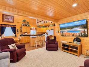 Interior acogedor de una cabaña con cocina, comedor y un amplio ventanal con vistas a un paisaje pintoresco.