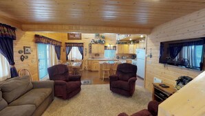 Ein Blockhaus-Interieur mit Wohnzimmer, Essbereich, Küche und einem an der Wand befestigten Fernseher.