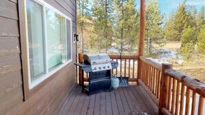 Eine Holterrasse mit Grill und Fenster mit Blick auf einen bewaldeten Bereich.