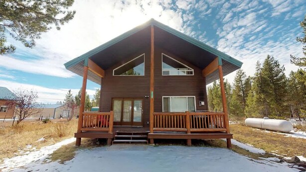 Eine zweistöckige Holzhütte mit Balkon, überdachter Veranda und freiem Blick auf den umliegenden Wald.