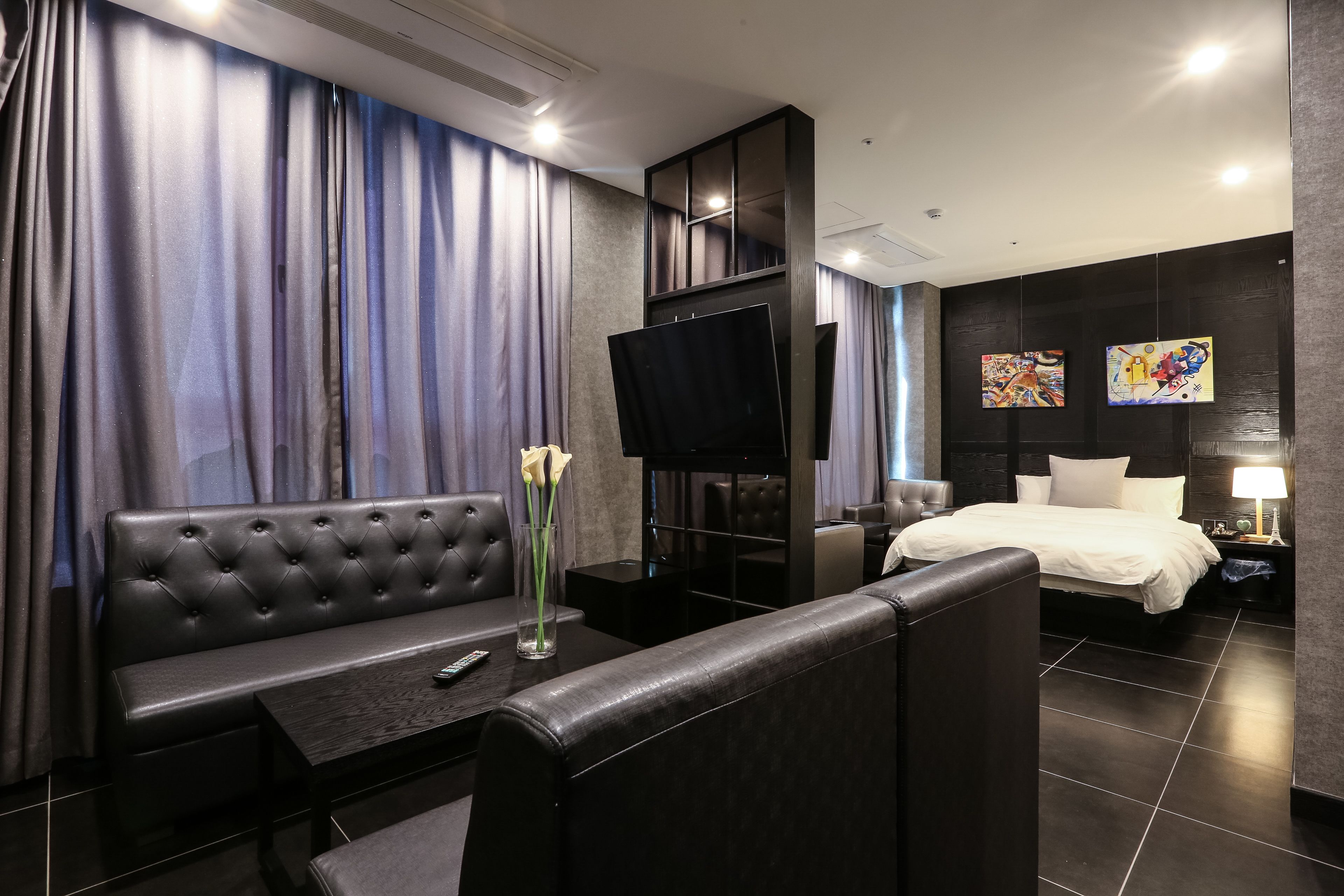 Una habitación de hotel moderna con un sofá, una cama, un televisor y obras de arte en las paredes.