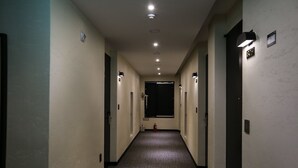 A narrow, well-lit hallway with a fire extinguisher and emergency exit sign on the wall. - Hotel Senne (Seoul)
