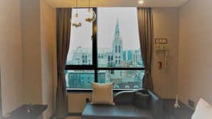 A hotel room with a large window offering a cityscape view, a bed, a sofa, and a small table with a decorative item. - Hotel Senne (Seoul)