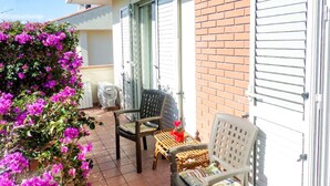 Un patio con dos sillas de mimbre y una mesa, rodeado por un muro de ladrillo y una valla blanca.