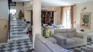 Una sala de estar con piso a cuadros, un sofá, una mesa de comedor con sillas y una escalera que lleva a otra habitación.