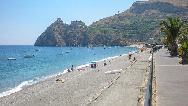 Una playa con barcos, gente y una colina rocosa al fondo.