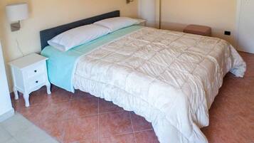 Una cama bien hecha con colcha blanca, una mesita de noche pequeña y una lámpara de pared.