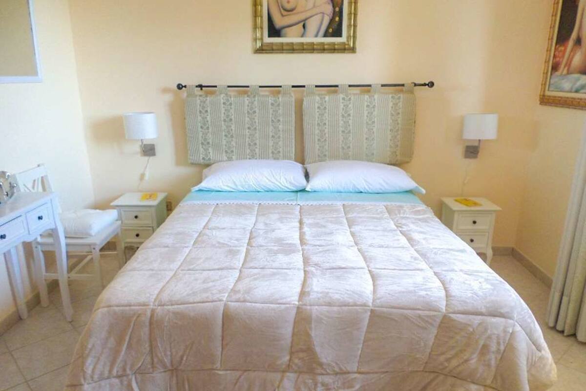 Un dormitorio con una cama grande, dos mesitas de noche, una mesita auxiliar y un escritorio con una silla.