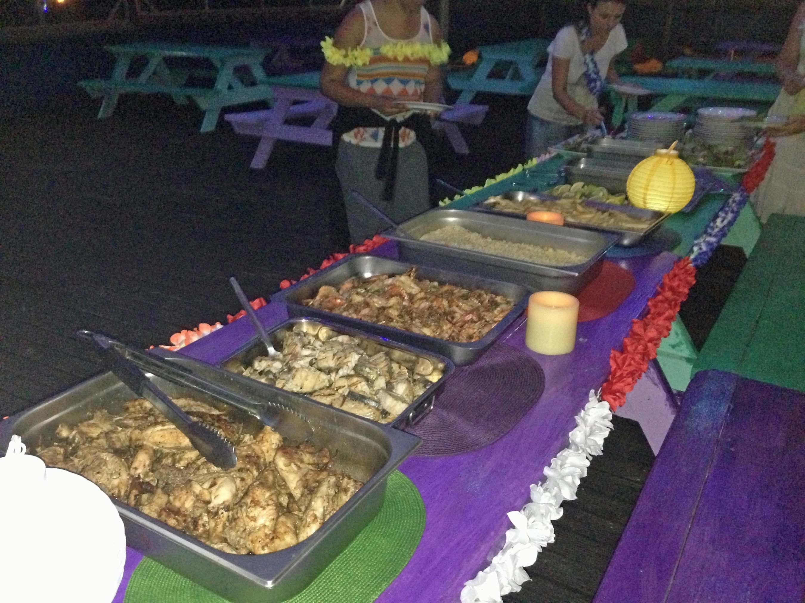 A buffet table with various dishes, including seafood and rice, set up outdoors at night.