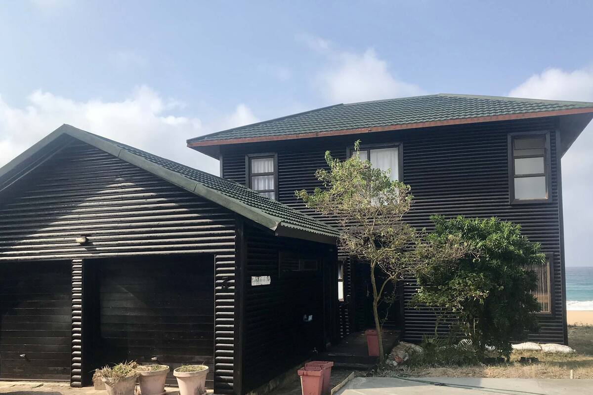 Um edifício à beira-mar com garagem e uma pequena árvore em frente.