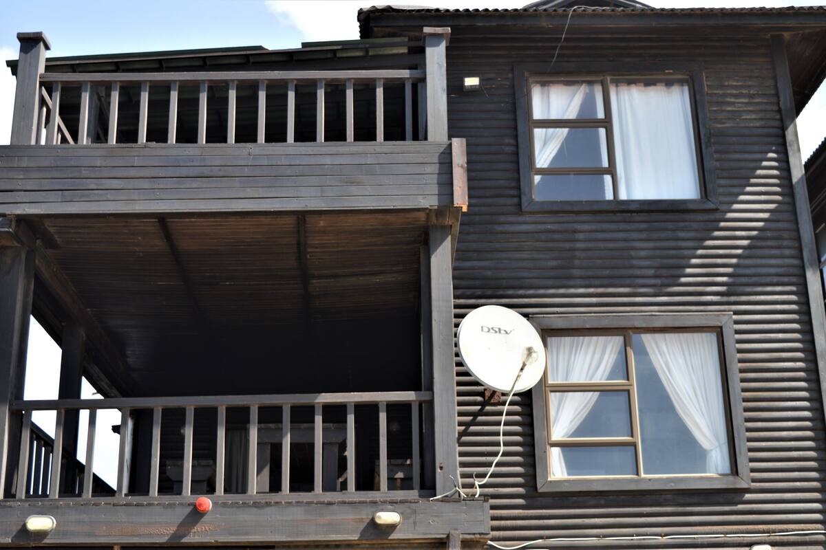 Uma casa de madeira de dois andares com varanda, antena parabólica e janela com cortinas.