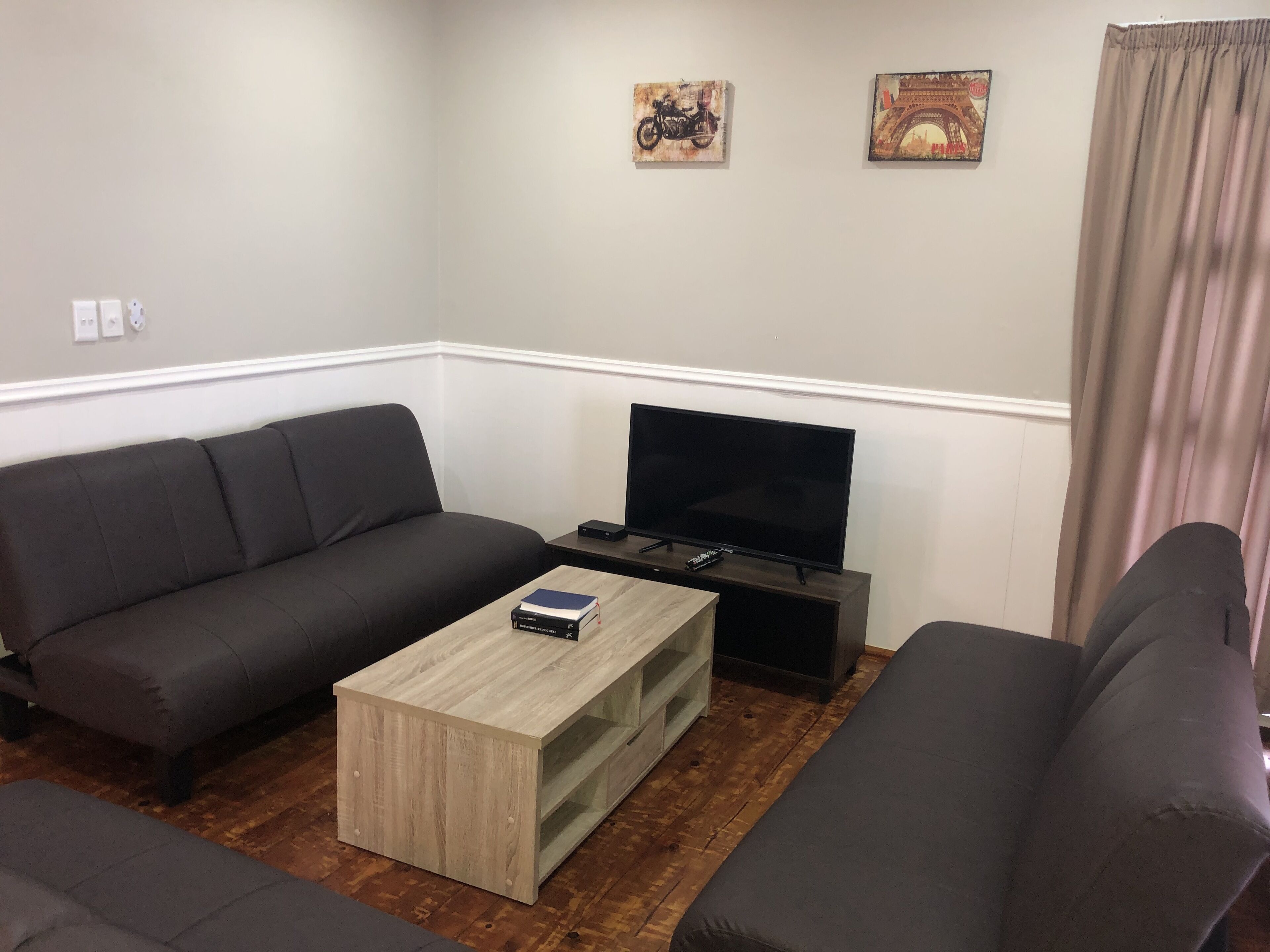 A living room with a dark grey sofa, a wooden coffee table, a flat-screen TV on a stand, and two wall-mounted pictures.