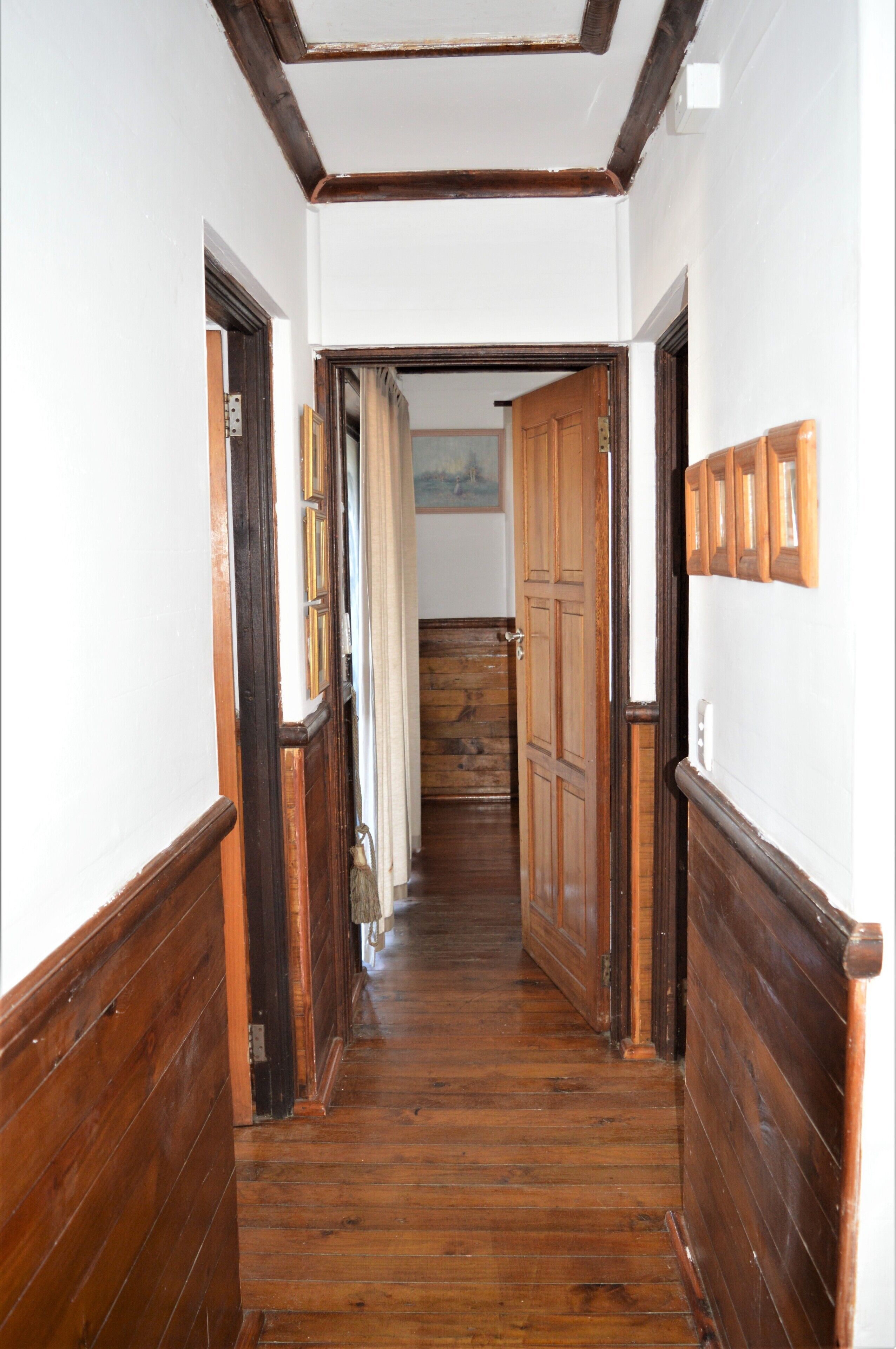 A hallway with wooden floors and walls, leading to a room with a door.