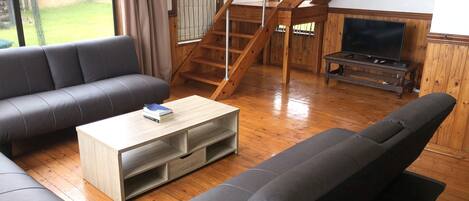 A living room with a wooden staircase, a sofa, a coffee table, and a television.