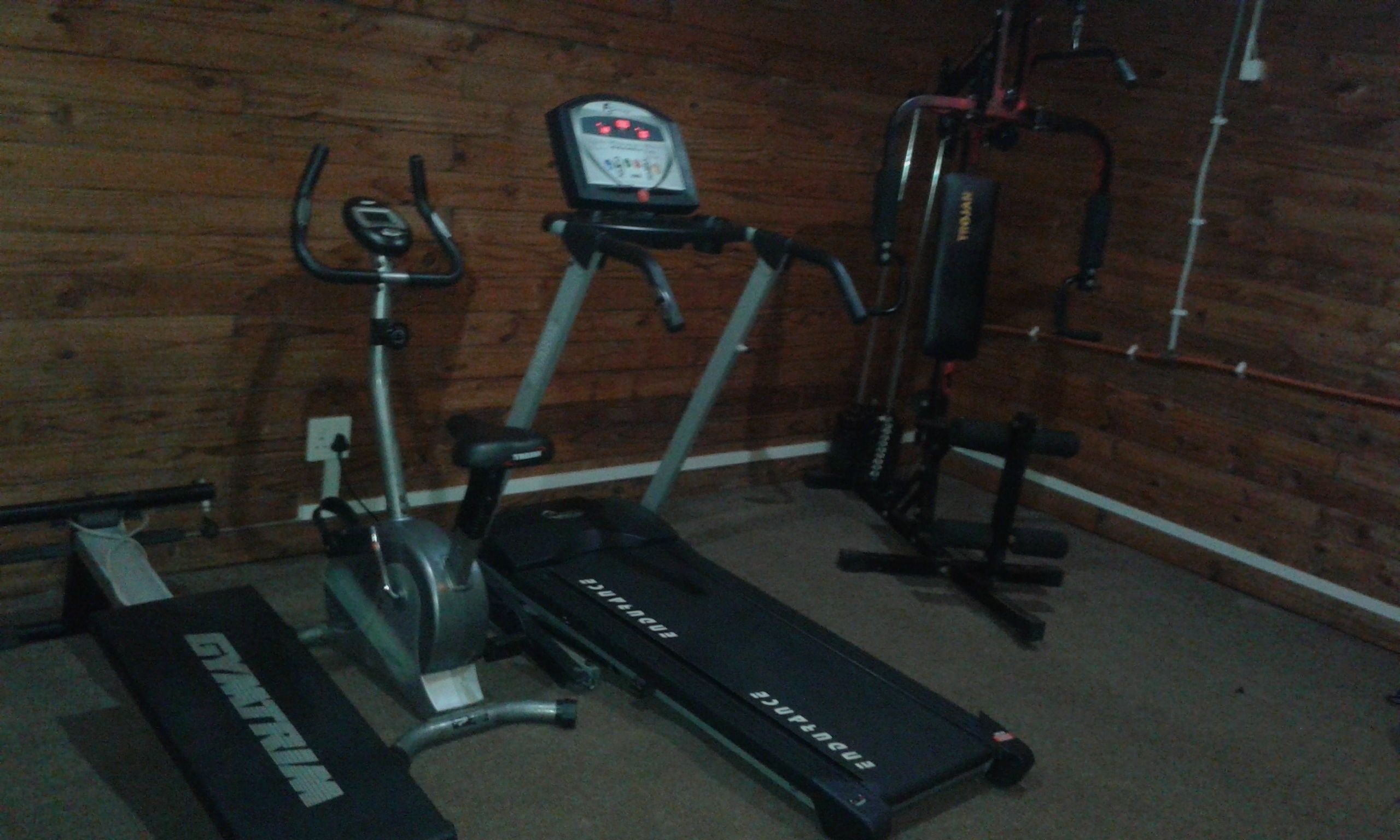 A home gym with a treadmill, elliptical, and weight machine.