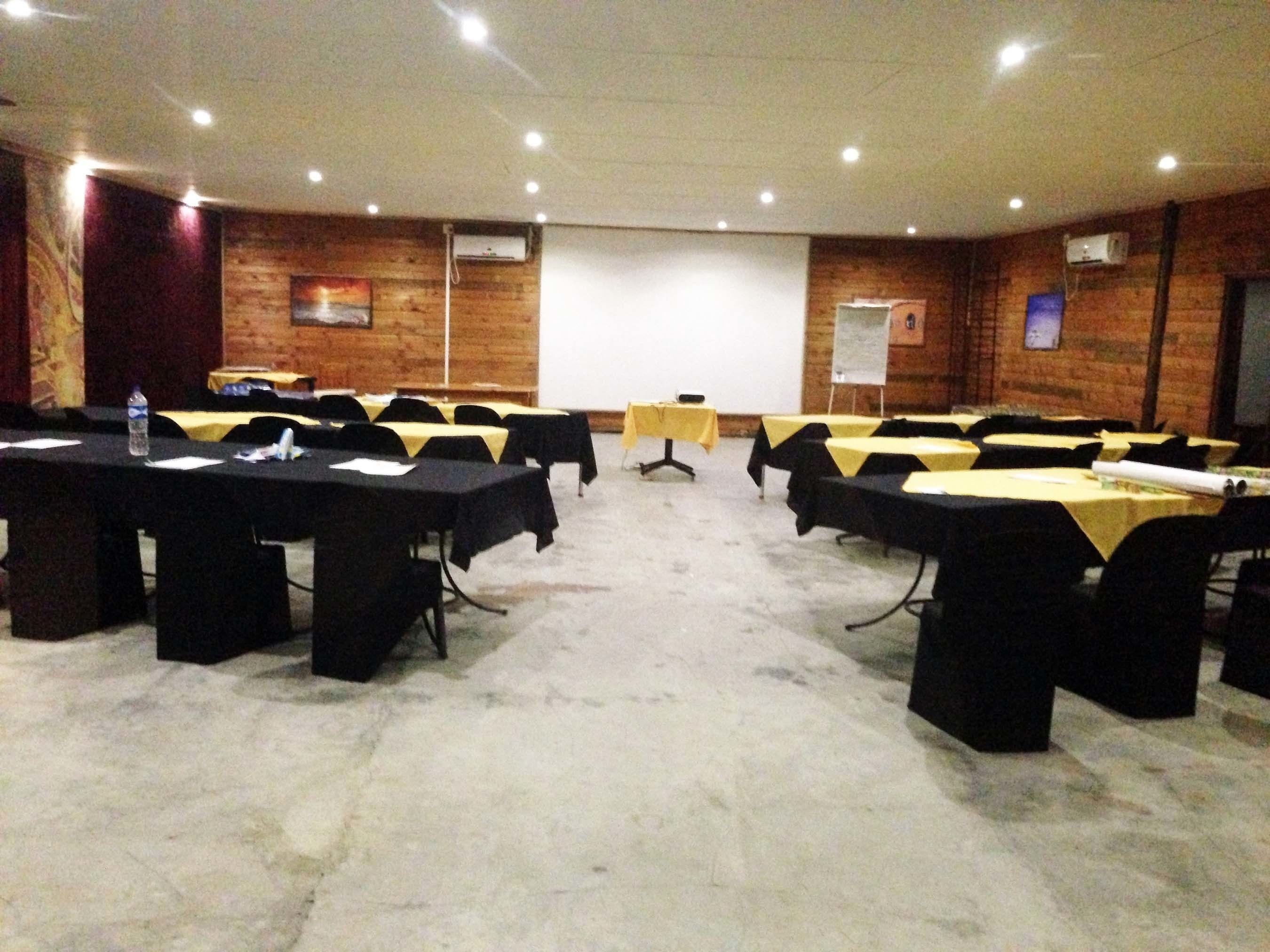 Uma sala de conferências com várias mesas, cadeiras e um projetor.