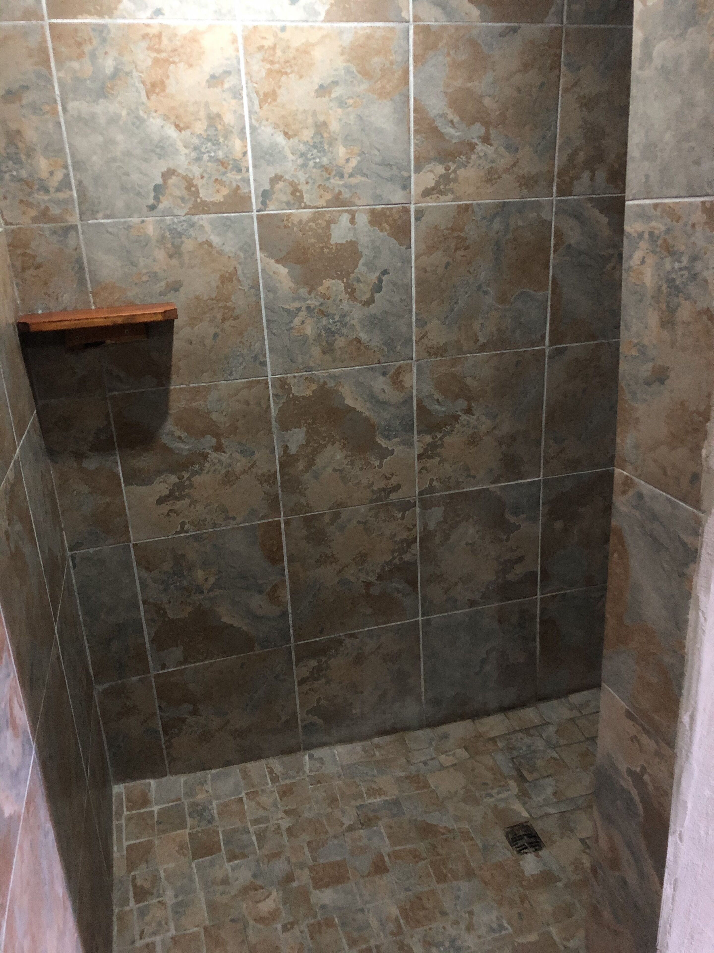 A shower area with stone tiles and a wooden shelf.