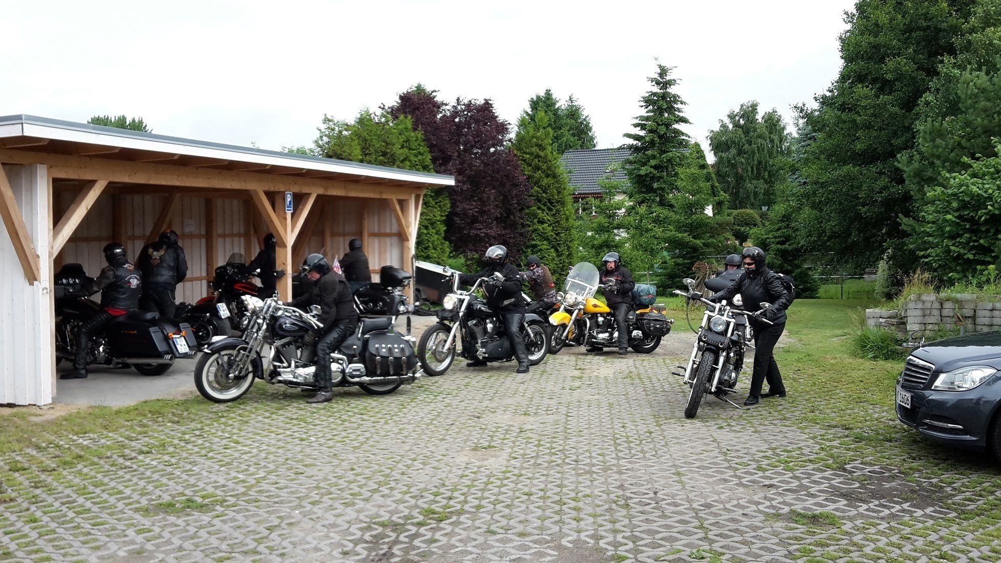 A covered outdoor area with motorcycles parked, a car, and a building with a wooden roof.