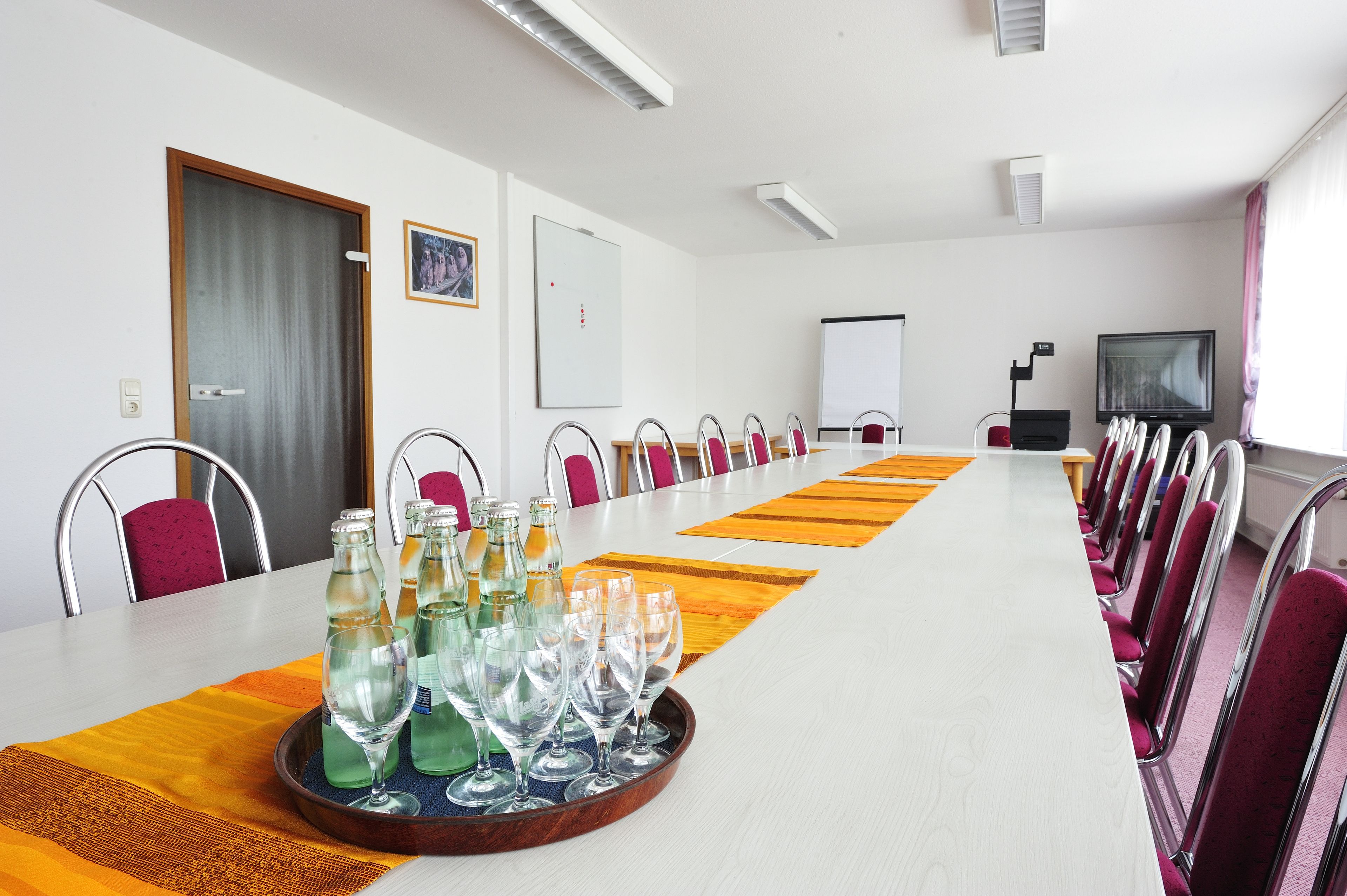 A conference room with a long table, chairs, a projector screen, and a television.